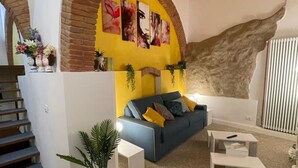 A modern living room with a blue sofa, white coffee tables, and a yellow mural on the wall.