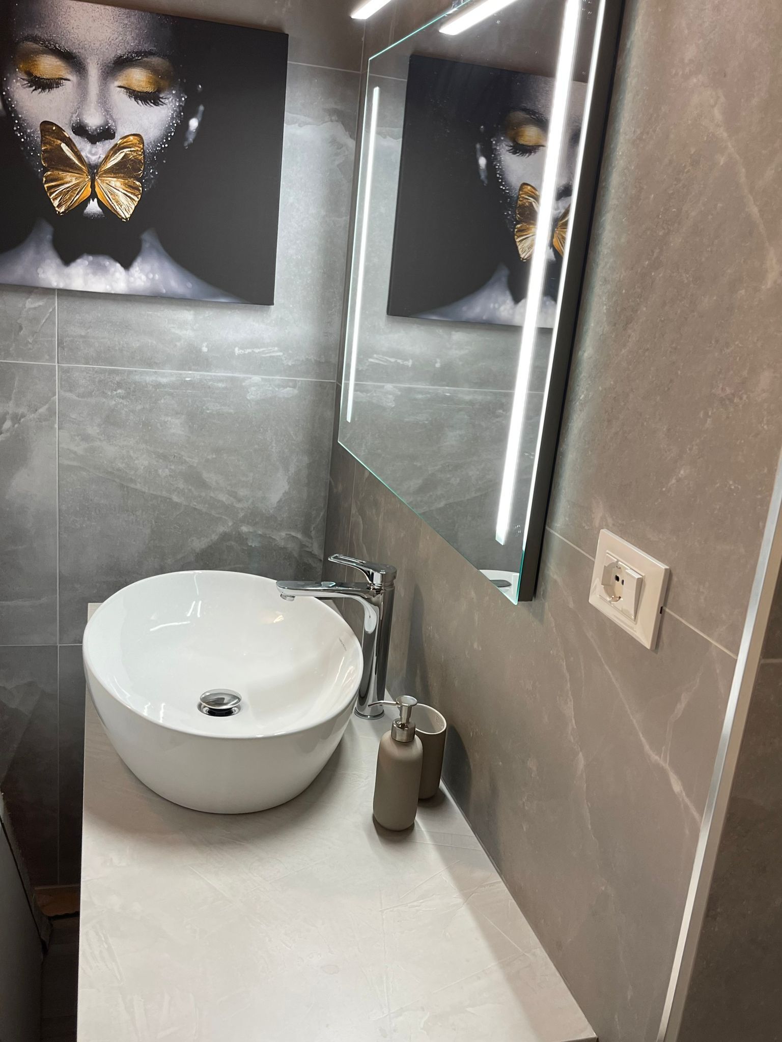 A modern bathroom with a large white sink, a mirror, and a wall-mounted light fixture.