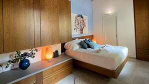 A bedroom with a wooden ceiling, a bed with pillows, a bedside table with a lamp, and a wall with a painting.