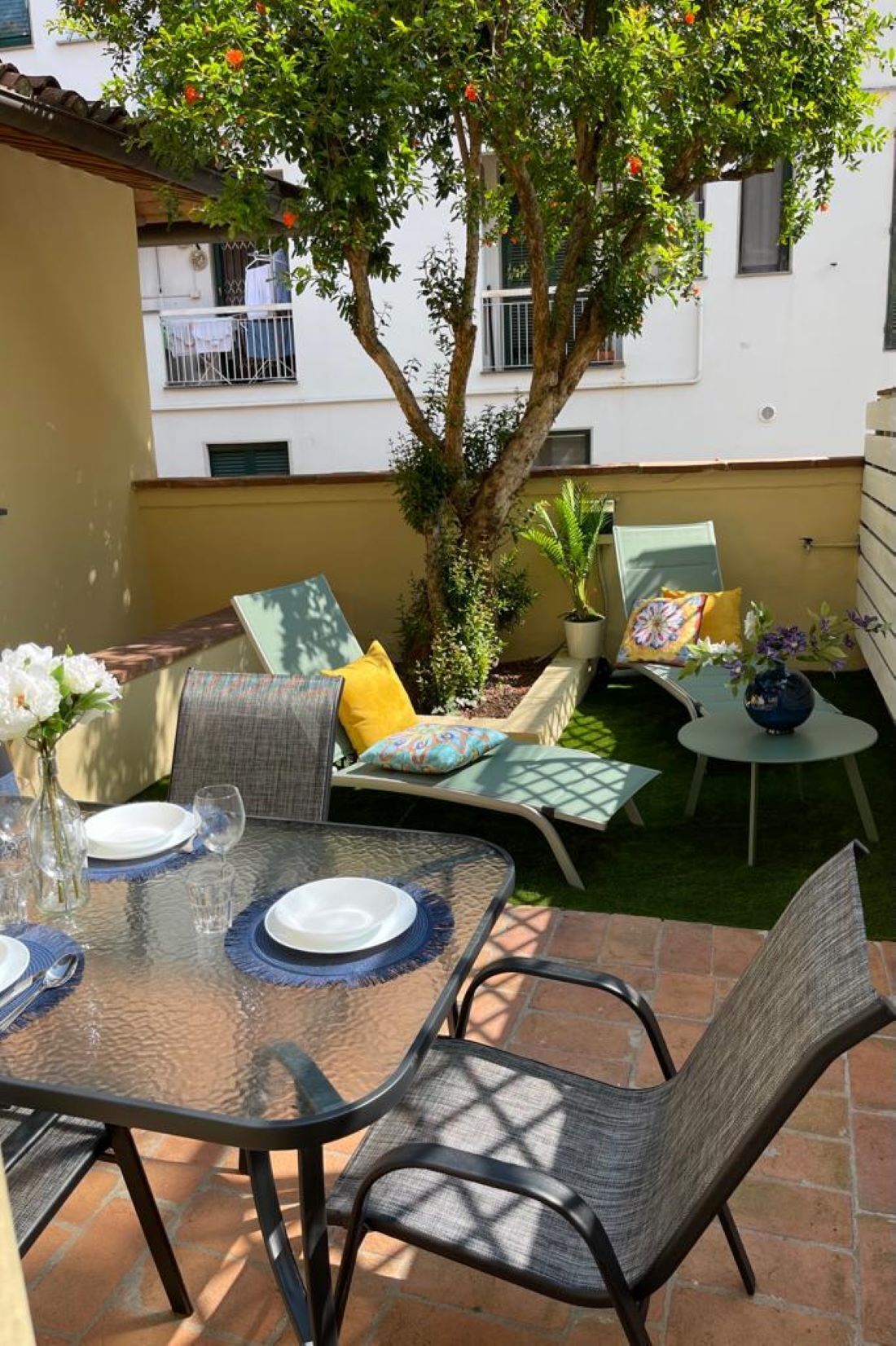 An outdoor patio with a table set for dining, cushioned seating, and a potted plant.