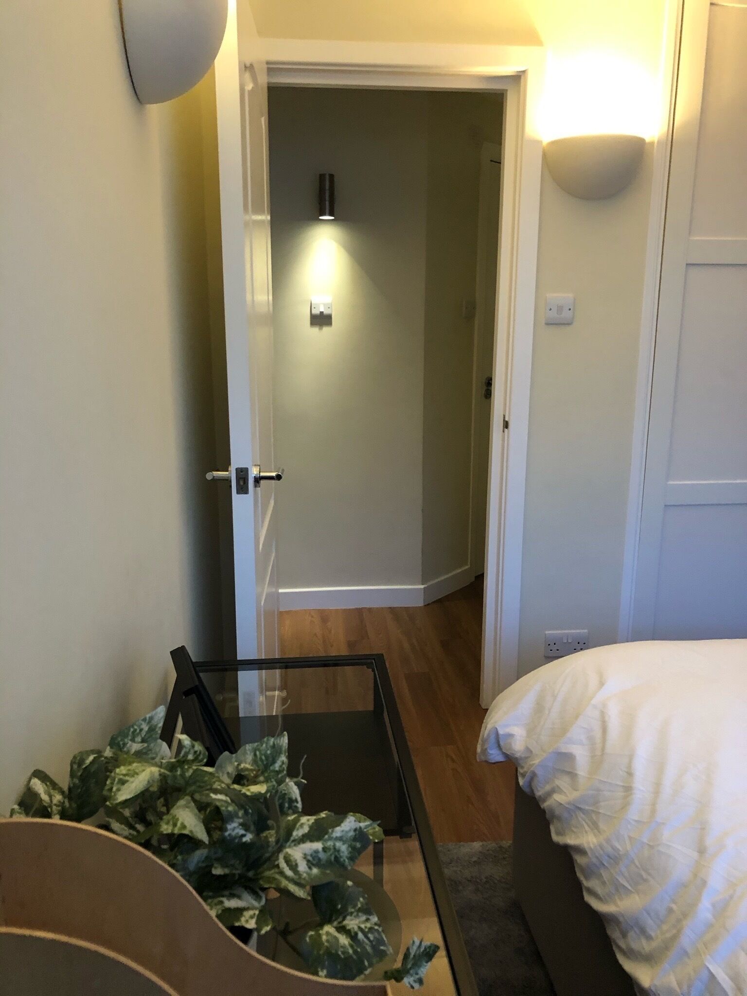Una habitación de hotel con una cama, una mesita con una planta y una puerta que da a otra habitación.