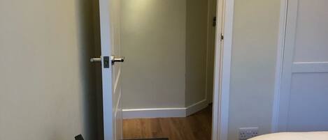 Una habitación de hotel con una cama, una mesita con una planta y una puerta que da a otra habitación.