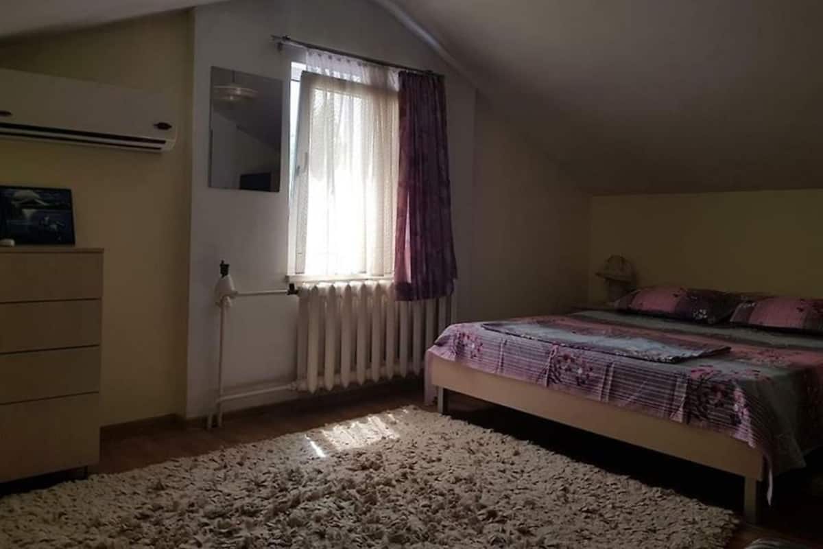 Quarto com cama, penteadeira, radiador e janela com cortinas.