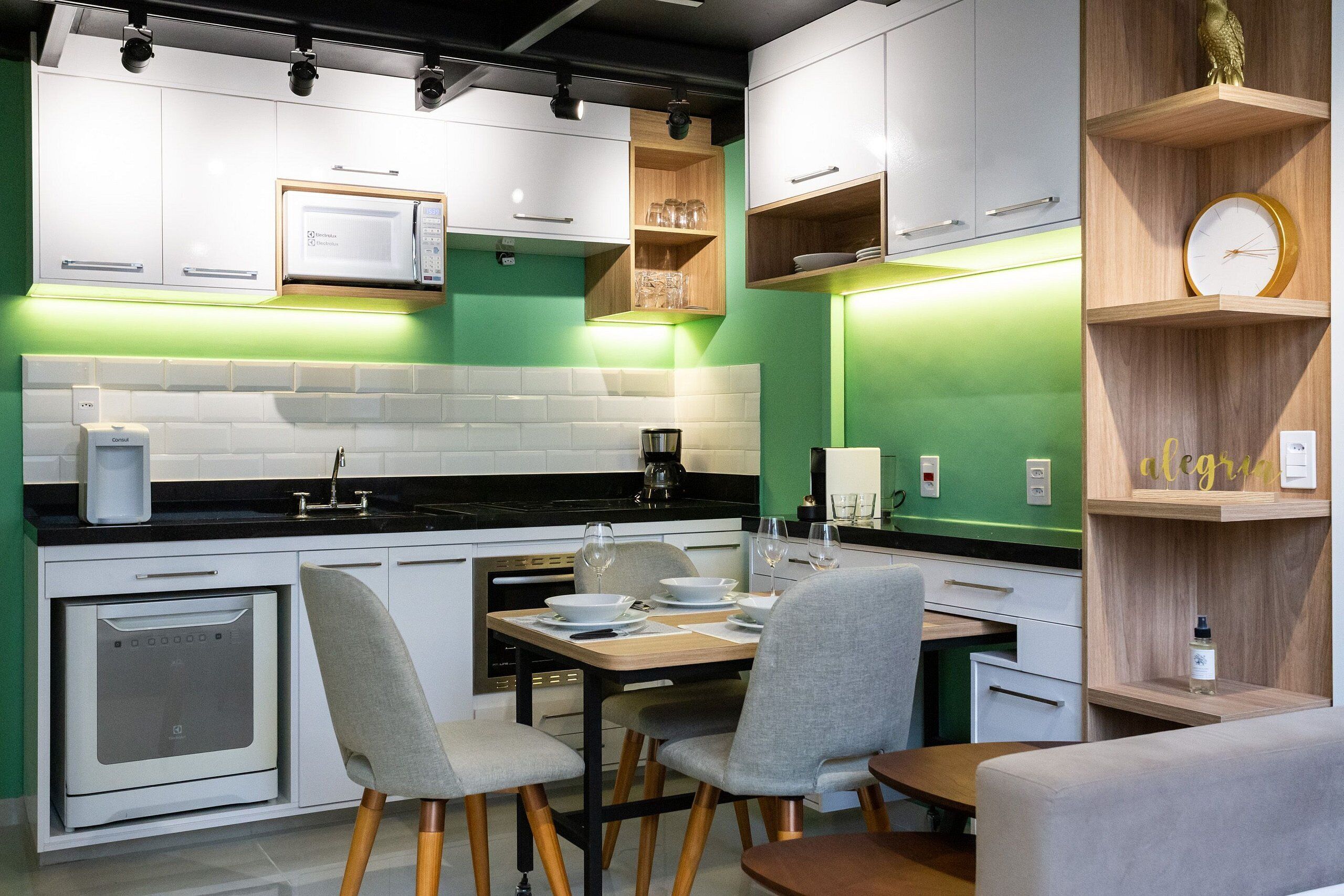 Een moderne keuken met witte kastjes, een magnetron, een koffieapparaat en een eethoek met een tafel en stoelen.