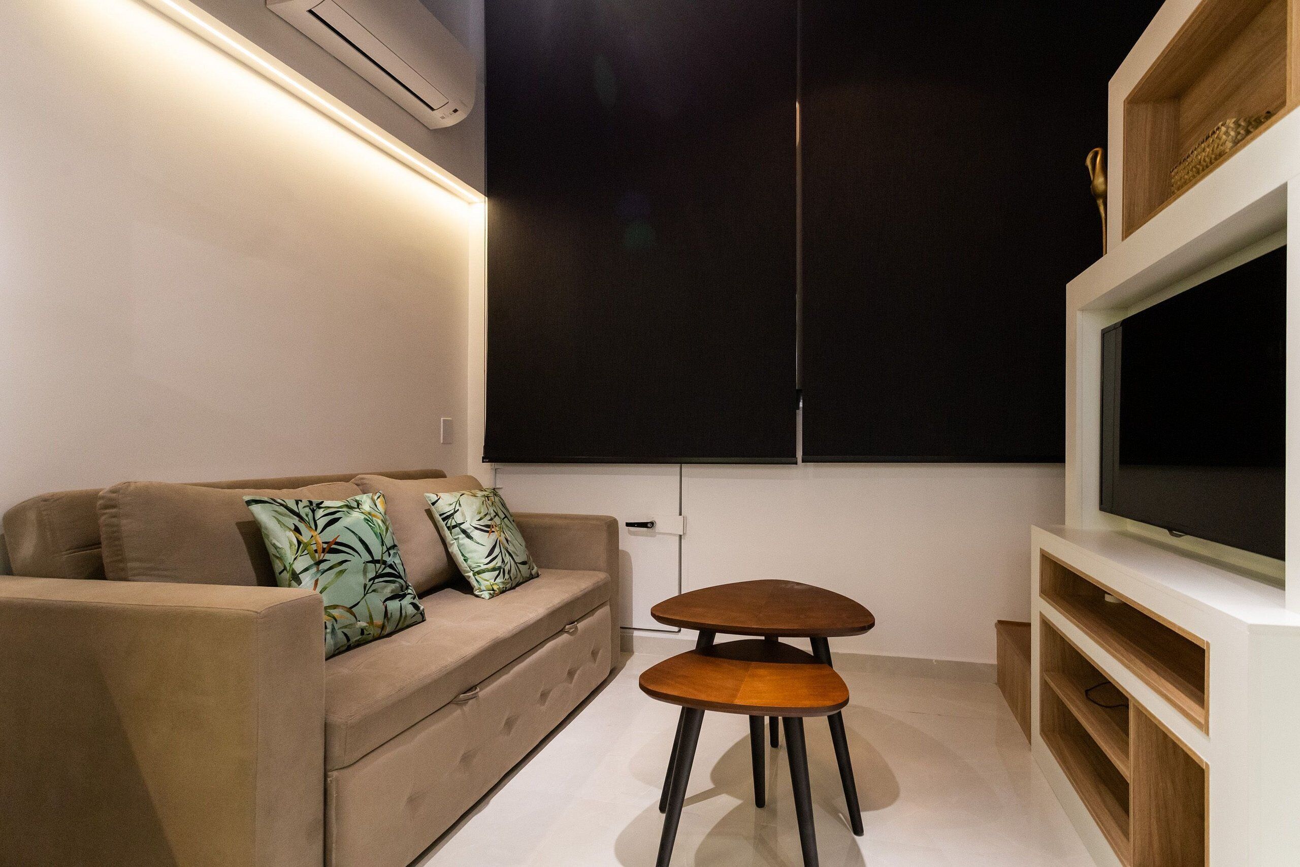 Uma sala de estar moderna com um sofá, uma pequena mesa de madeira e uma TV fixada na parede.