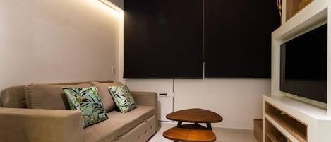 Uma sala de estar moderna com um sofá, uma pequena mesa de madeira e uma TV fixada na parede.