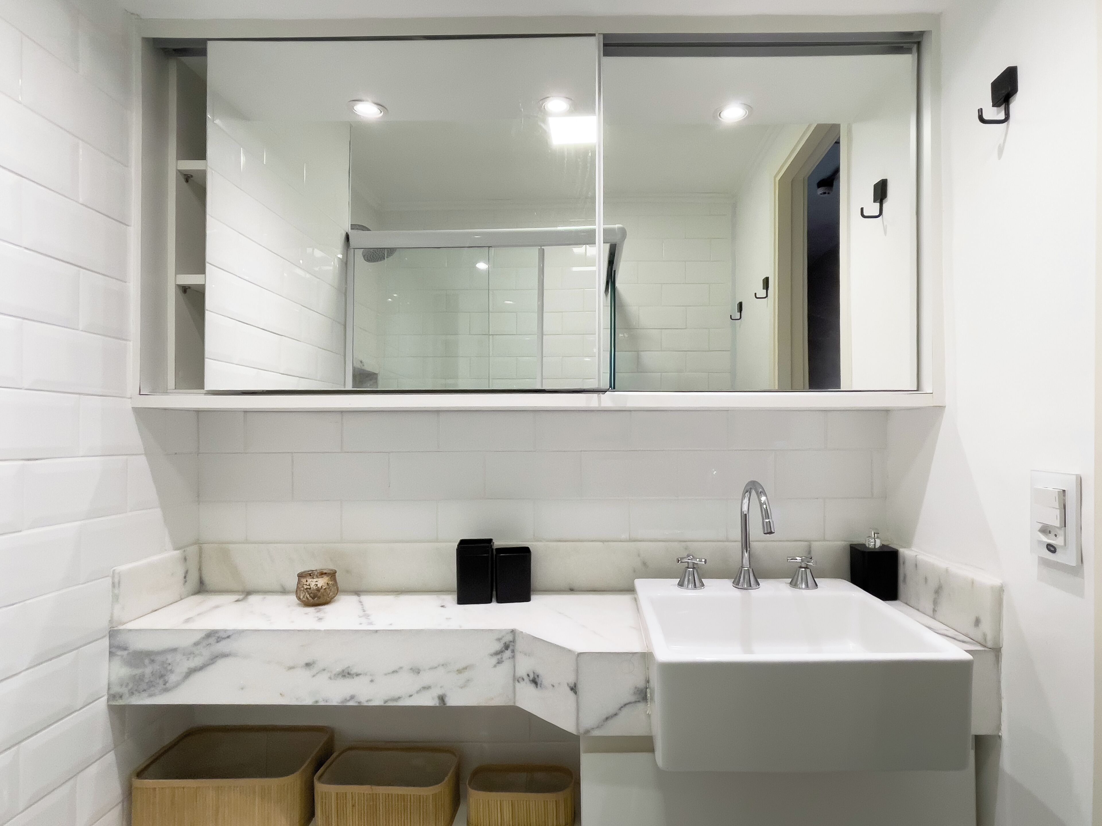 A modern bathroom with a large mirror, white tiles, a marble countertop, and a sink with two faucets.