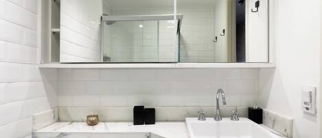 A modern bathroom with a large mirror, white tiles, a marble countertop, and a sink with two faucets.