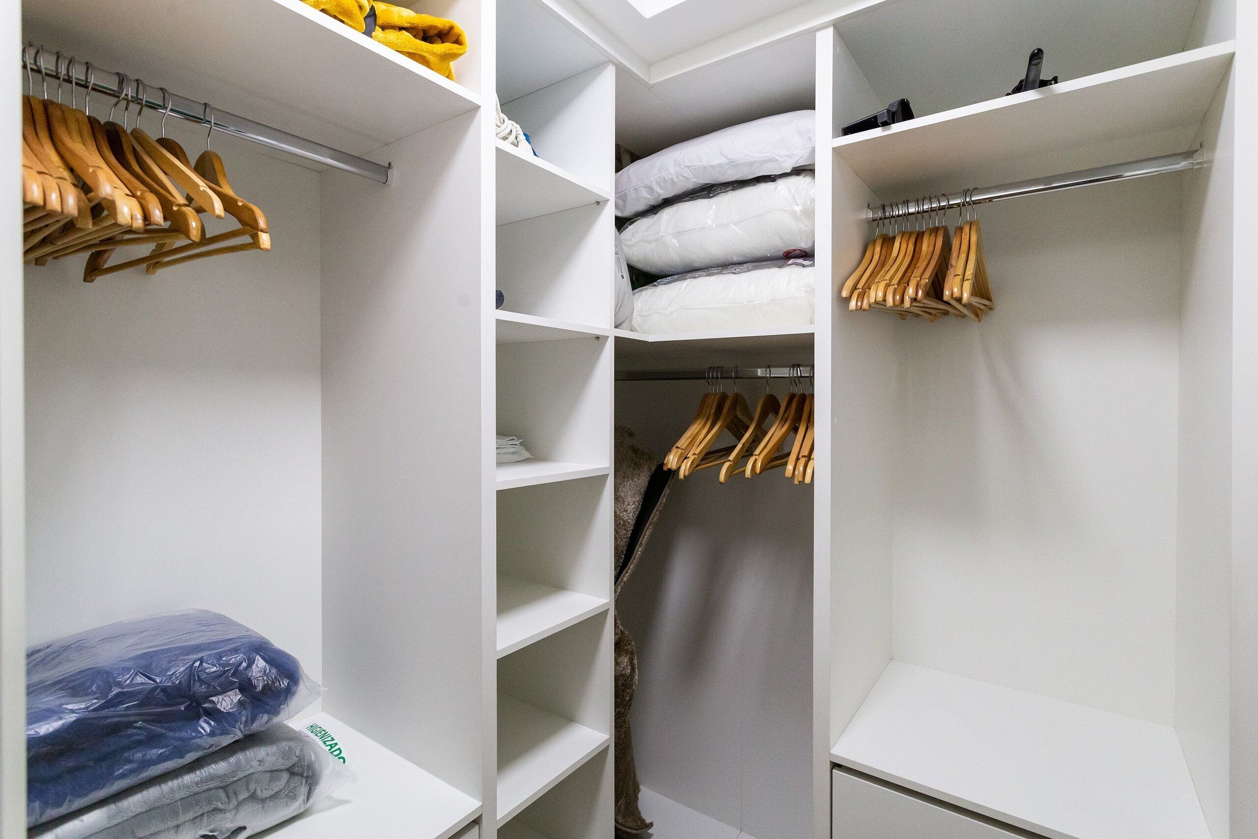A walk-in closet with wooden hangers, shelves, and a vacuum cleaner.