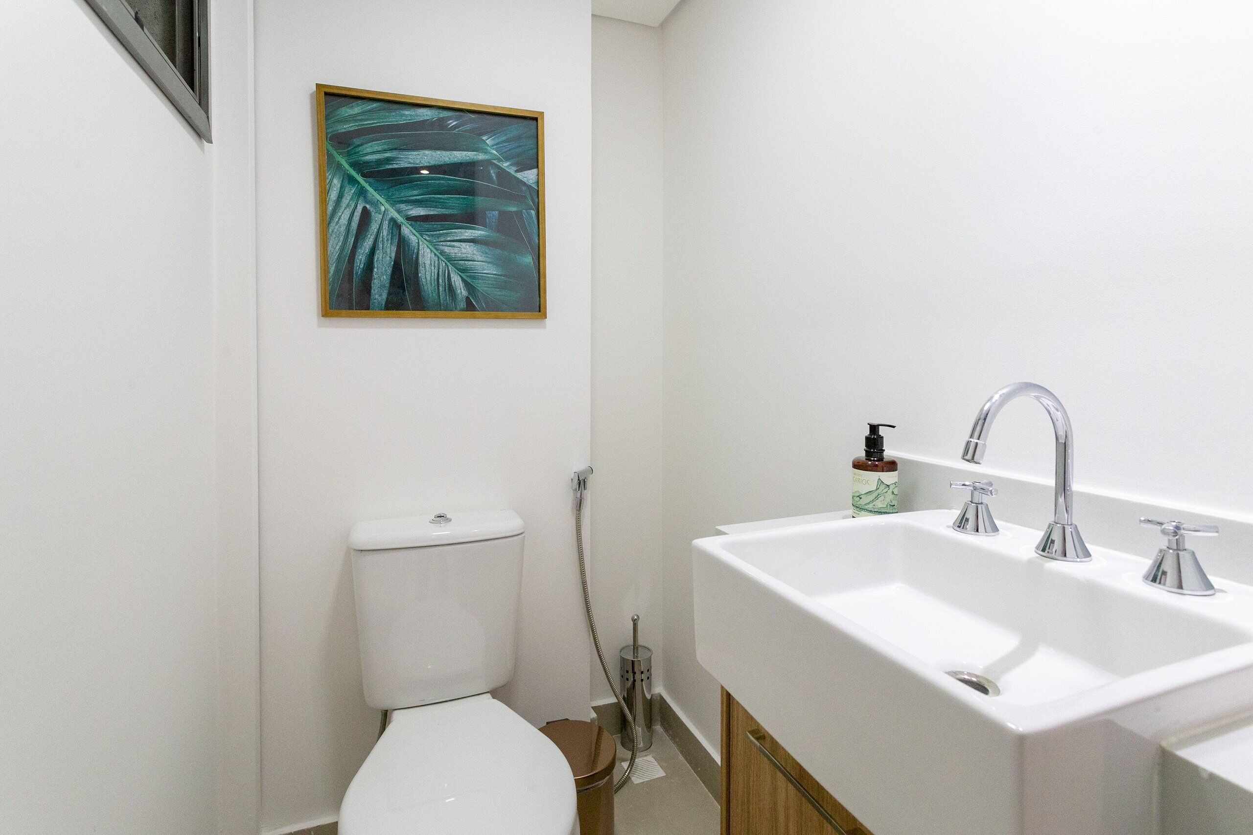 A bathroom with a white toilet, a sink with a mirror, and a framed tropical leaf artwork on the wall.