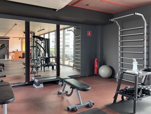 Une salle de sport équipée de matériel d’exercice, d’un banc, d’un support à squats et d’un grand miroir.