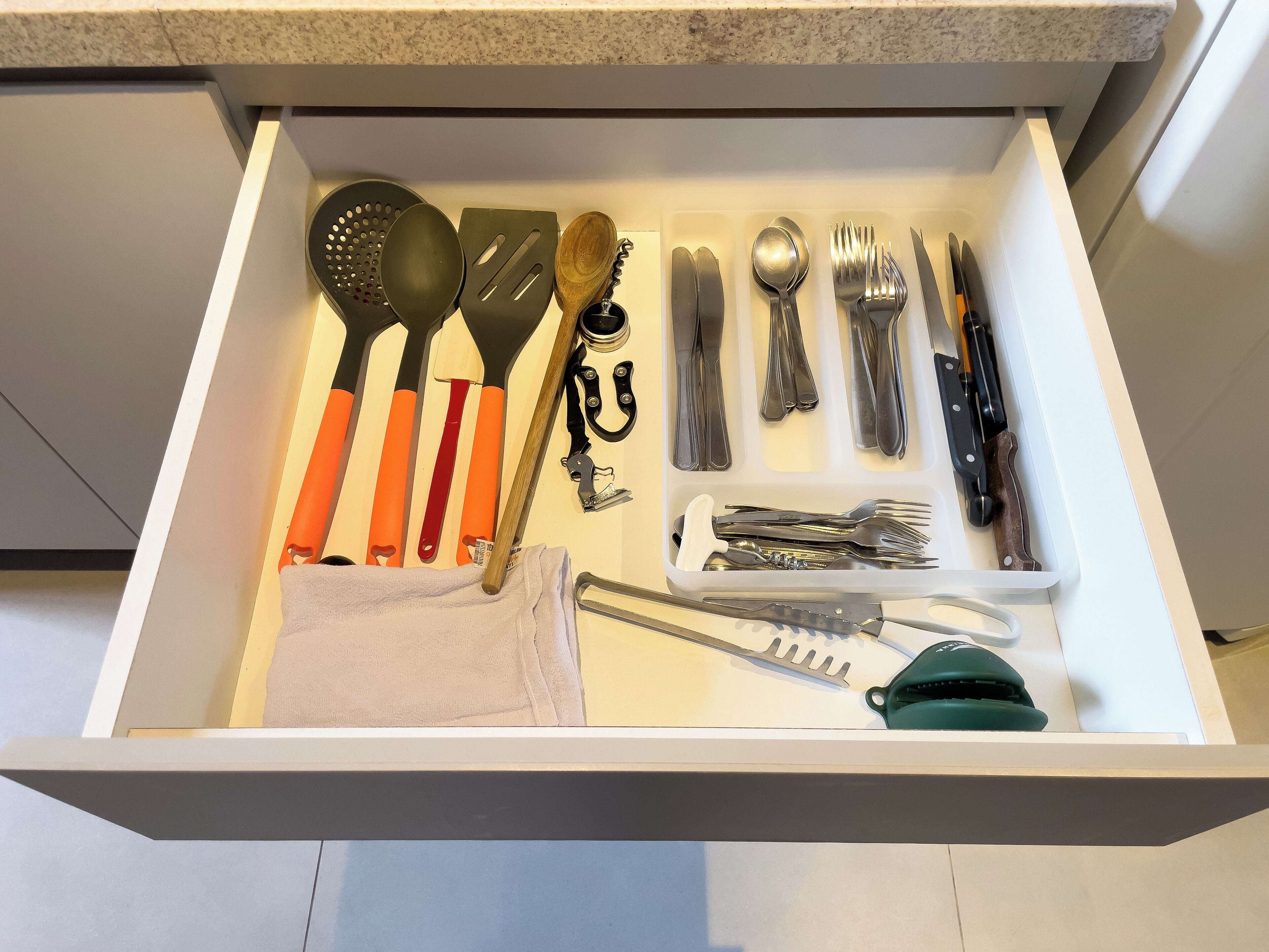 A drawer containing various kitchen utensils including spatulas, tongs, and a green-handled utensil.