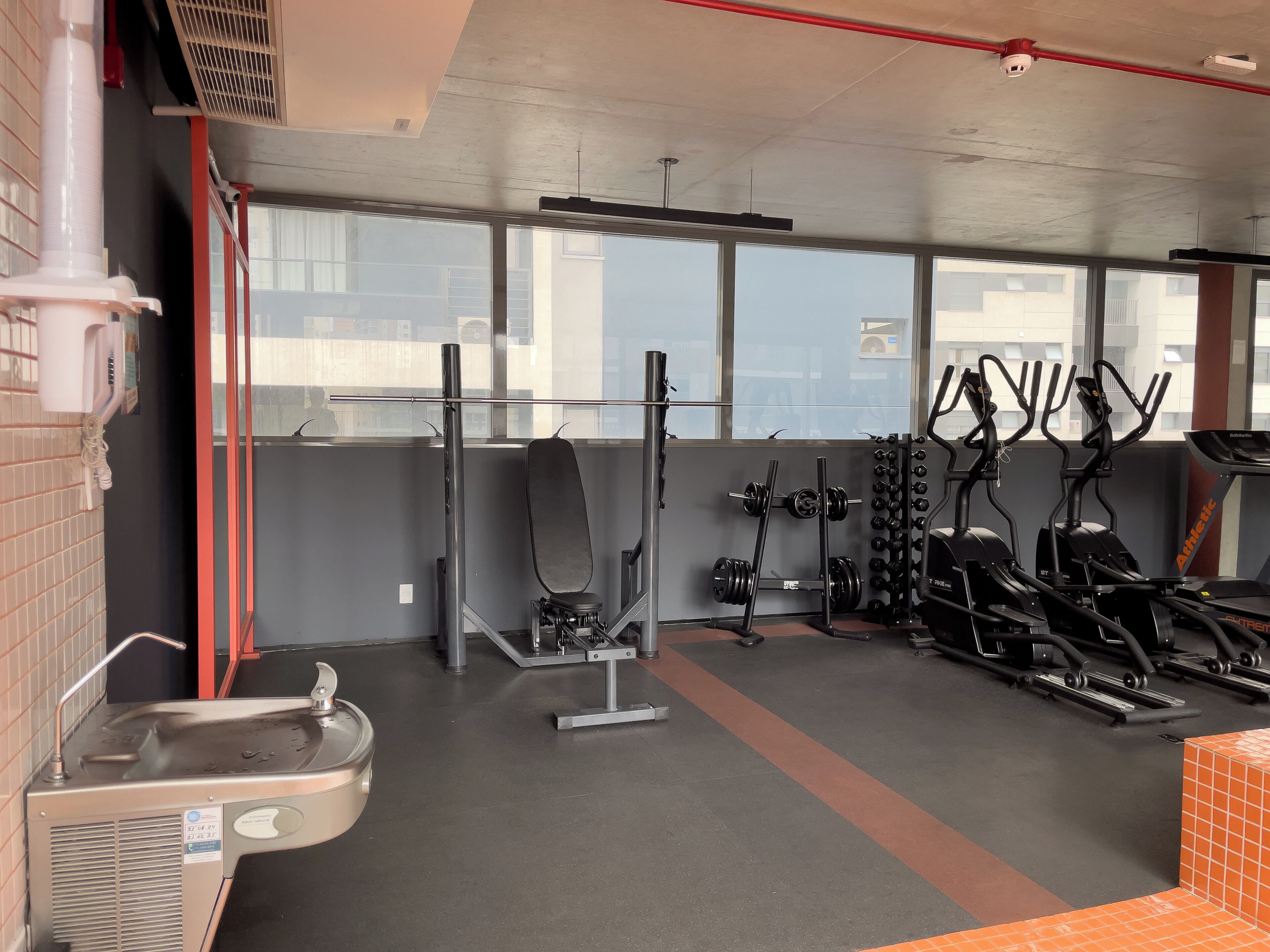 Un gimnasio con equipo de levantamiento de pesas, cintas de correr y un dispensador de agua.