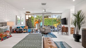 A modern living room with a large bed, sofa, and a dining area with a TV and plant. - The Desert Breeze at Sandpiper; Completely remodeled with private spa! (Palm Desert)
