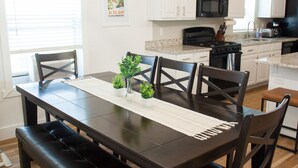 Une cuisine moderne avec des meubles blancs, une table à manger en bois foncé et un luminaire suspendu.