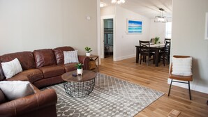 Un salon avec un canapé en cuir marron, une table basse et un tapis à motifs. On aperçoit à l’arrière-plan un coin repas avec une table et des chaises.