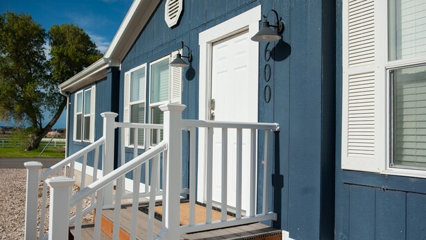 Une maison bleue avec des volets blancs, une porte blanche et une terrasse en bois dotée de balustrades blanches.