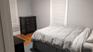 A bedroom with a bed, a dresser, and a window with blinds.