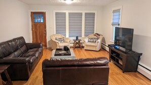A living room with a brown leather sofa, two armchairs, a coffee table, and a TV on a stand.