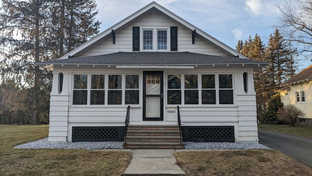 A two-story house with a gabled roof, large windows, and a front porch with steps.