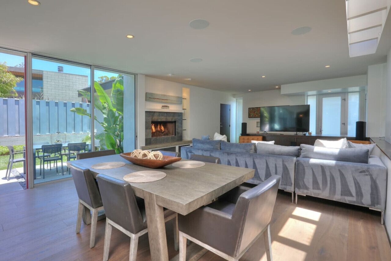 A modern living room with a fireplace, a dining area with a table and chairs, and a large TV.
