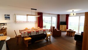Ein gemütliches Wohnzimmer mit einem Holzesstisch, einem Fernseher und einem großen Fenster mit Vorhängen.