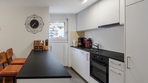 Ett modernt kök med en svart bänkskiva, vita skåp och en inbyggd ugn. Det finns ett fönster med utsikt över byggnaderna utanför.