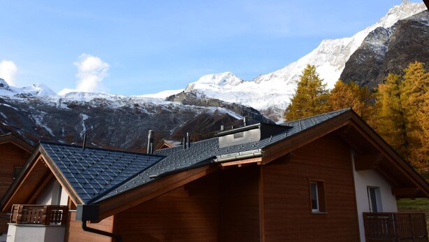 Una cabana de fusta amb teulada inclinada, amb muntanyes nevades i fullatge d'autorriu al fons.