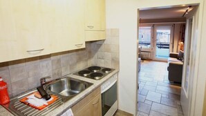 Una cucina con un fornello, un lavandino e degli armadietti. Sul bancone c'è una bottiglia rossa.
