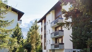 Een meerlaags woongebouw met balkons, omgeven door bomen en een berg op de achtergrond.