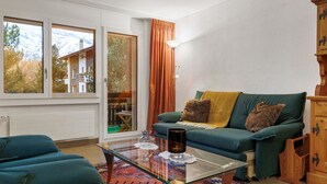 Ein Wohnzimmer mit einem grünen Sofa, einem Glastisch und einem gemusterten Teppich.