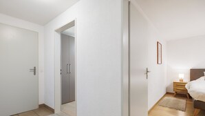 Ein modernes Schlafzimmer mit Holzboden, einem Bett mit Kopfteil, einem Nachttisch mit Lampe und einer Tür zu einem weiteren Raum.