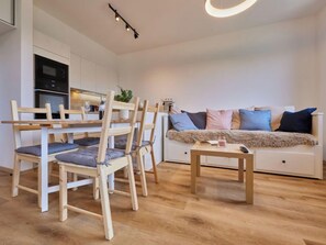 Un espacio habitable compacto con kitchenette, un sofá con cojines y una zona de comedor con sillas.