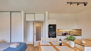 Una habitación de hotel moderna y compacta con cama, una pequeña mesa de comedor y una kitchenette.