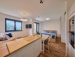Una habitación moderna y bien iluminada, con una mesa de comedor de madera, una cama con ropa de cama azul y un televisor montado en la pared.