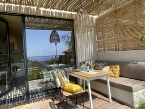 Un patio moderno al aire libre con una puerta de vidrio que da a una cocina, un comedor con mesa y sillas, y un sofá con cojines.