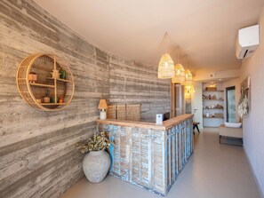 Un espace d'accueil comprenant un comptoir de réception en bois, une étagère ronde en osier et une grande plante en pot.