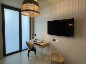 Una camera moderna con una grande TV a parete, una scrivania in legno, una sedia, uno sgabello e un'ampia finestra con vista.