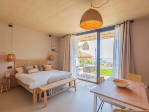 Une chambre à coucher comprenant un lit, des tables de chevet, un banc et une table à manger, avec vue sur l’extérieur.