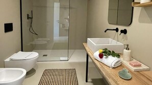 A modern bathroom with a glass shower enclosure, a white toilet, a bidet, and a wooden vanity with a sink and towel rack. - Casa Mia 4 by Interhome (San Lorenzo al Mare)