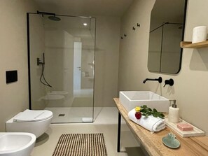Un bagno moderno con box doccia in vetro, un water bianco, un bidet e un mobile bagno in legno con lavandino e porta asciugamani.