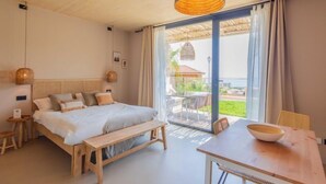 Een slaapkamer met een bed, nachtkastjes, een bankje, een eettafel en uitzicht op de omgeving.