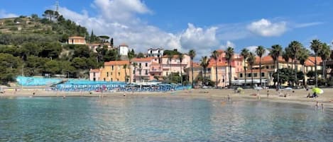 A coastal town with clear waters, beach umbrellas, and buildings with red roofs.