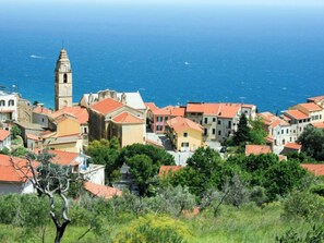 Un pueblo costero con arquitectura mediterránea tradicional, que incluye un campanario destacado y edificios con tejados de teja.
