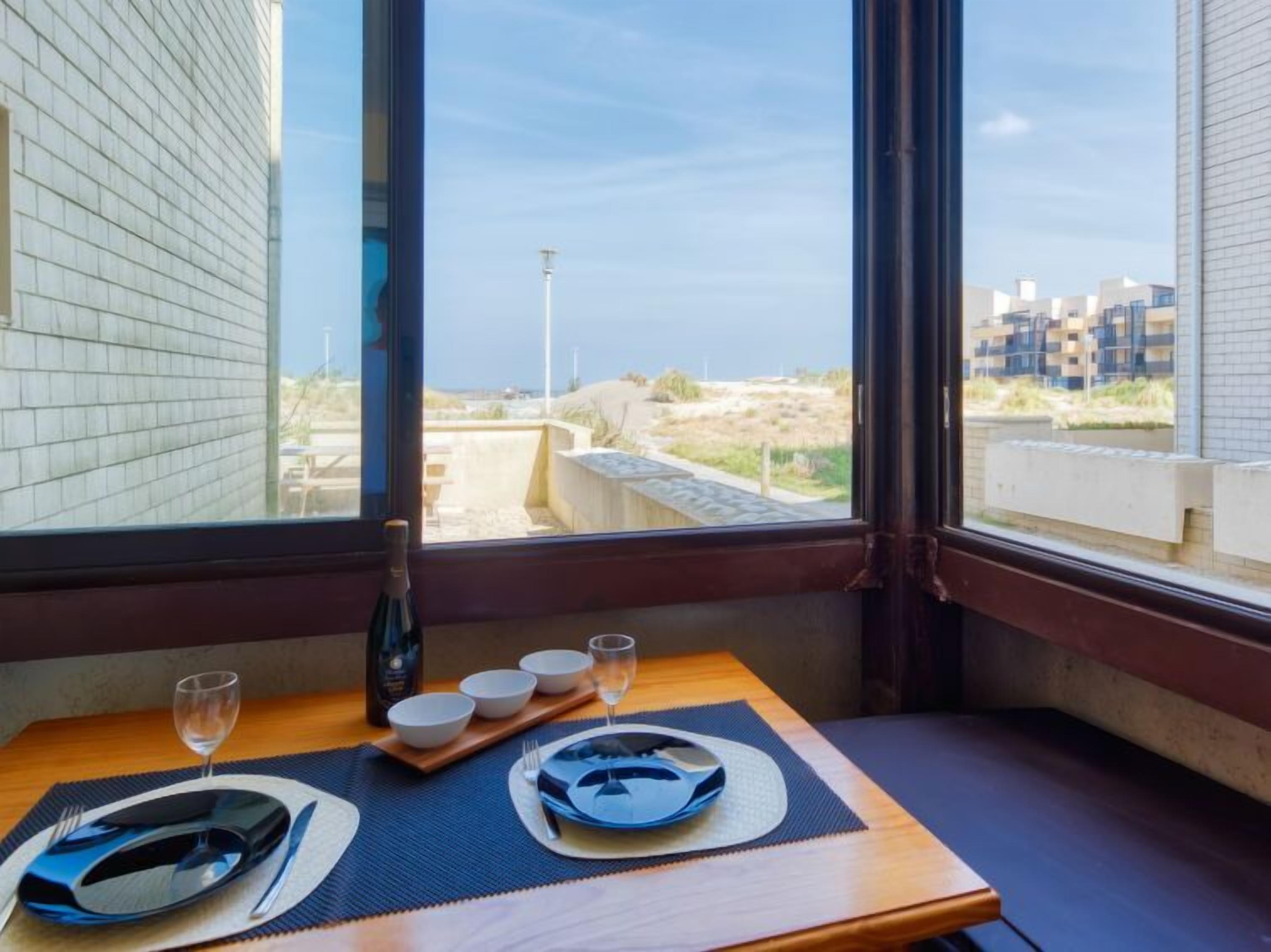 Una mesa de comedor dispuesta con platos, cuencos y cubiertos, con una botella y vasos encima.