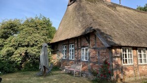 A traditional thatched-roof house with a brick exterior, a chimney, and a small garden with a bench and a covered table. - Reethuus by Interhome (Sandbostel)
