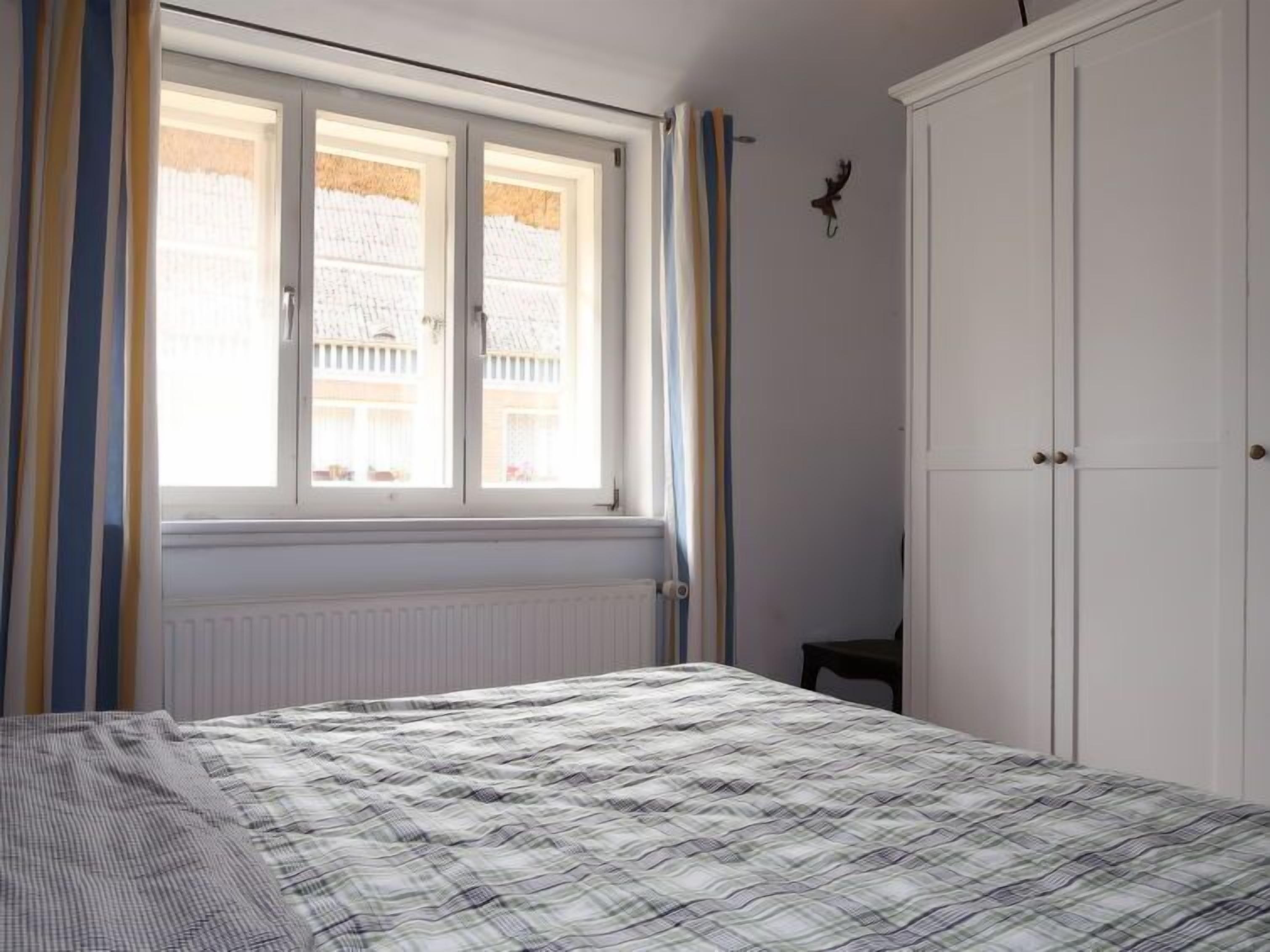 A bedroom with a bed, a window with curtains, a radiator, and a wardrobe.
