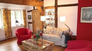A cozy living room with a wooden ceiling, a red armchair, a white sofa, and a glass coffee table. - Reethuus by Interhome (Sandbostel)