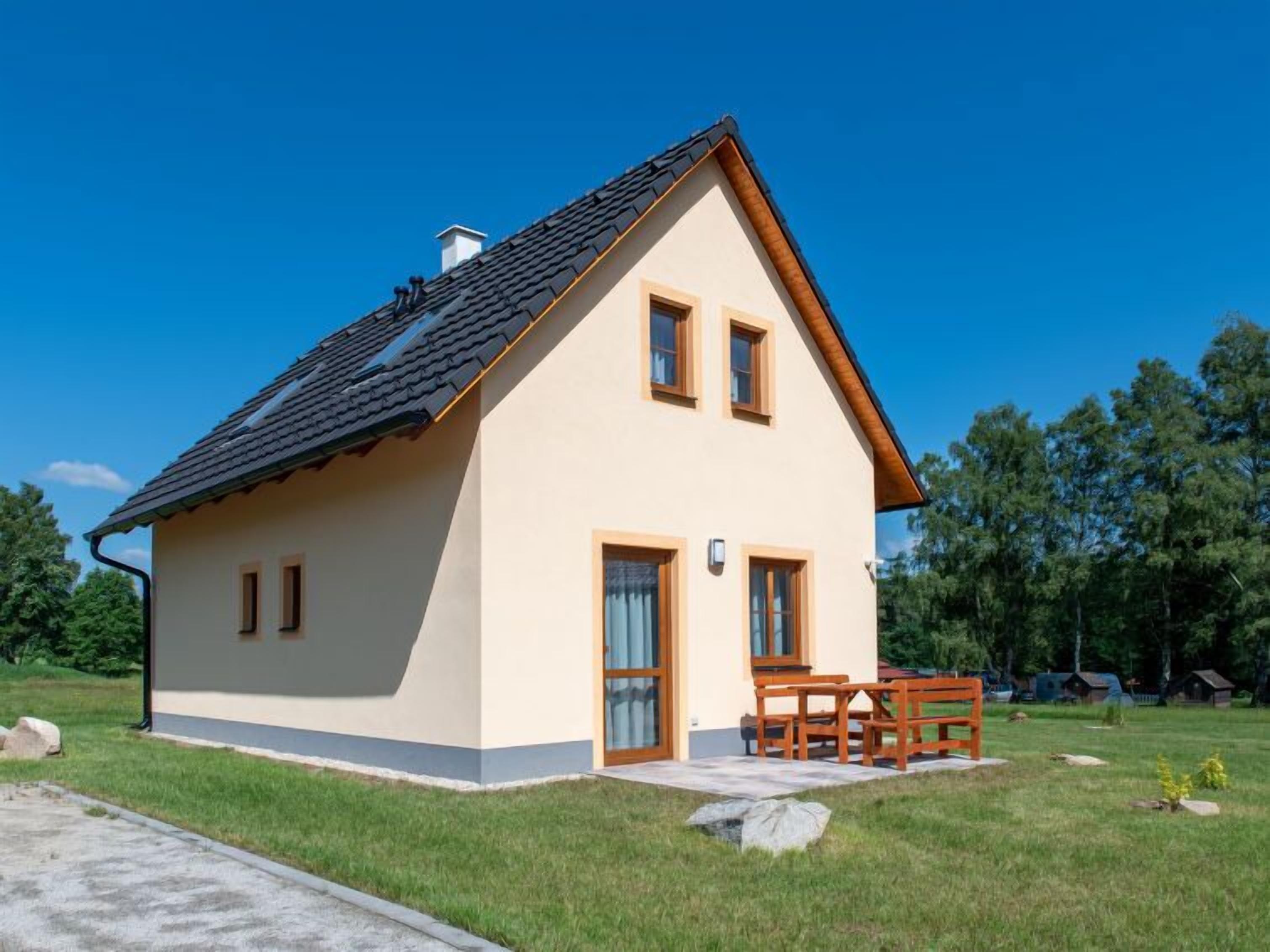 Una casa a due piani con tetto spiovente, un portico con mobili in legno e un prato curato.