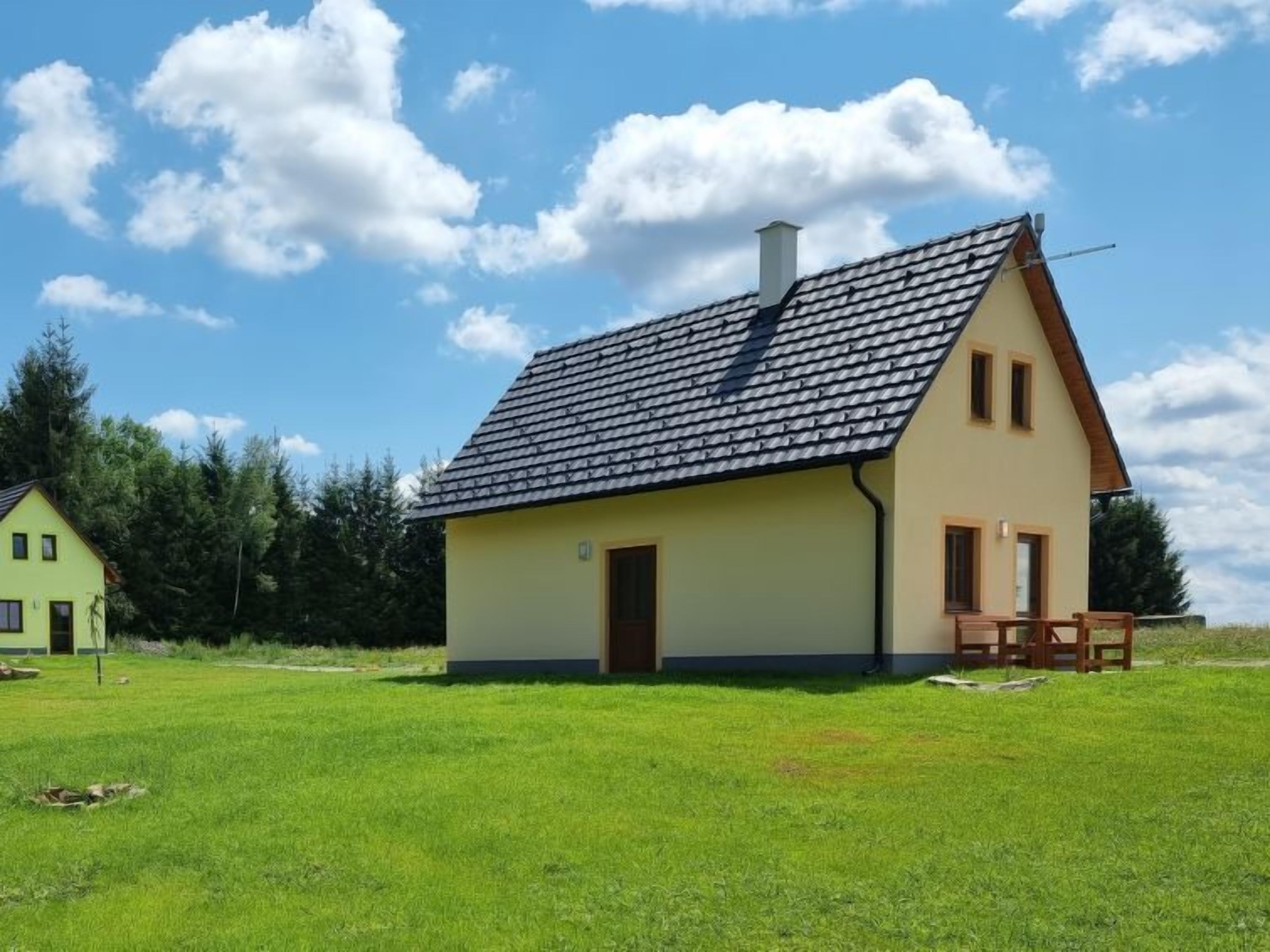 A single-story house with a sloped roof, a chimney, and a small porch with a bench.